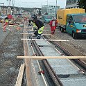Coulage d'une semelle de goudron sous les rails pour l'insonorisation, avant de les prendre dans le béton.